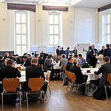 Personen sitzen an runden Tischen in einer Halle