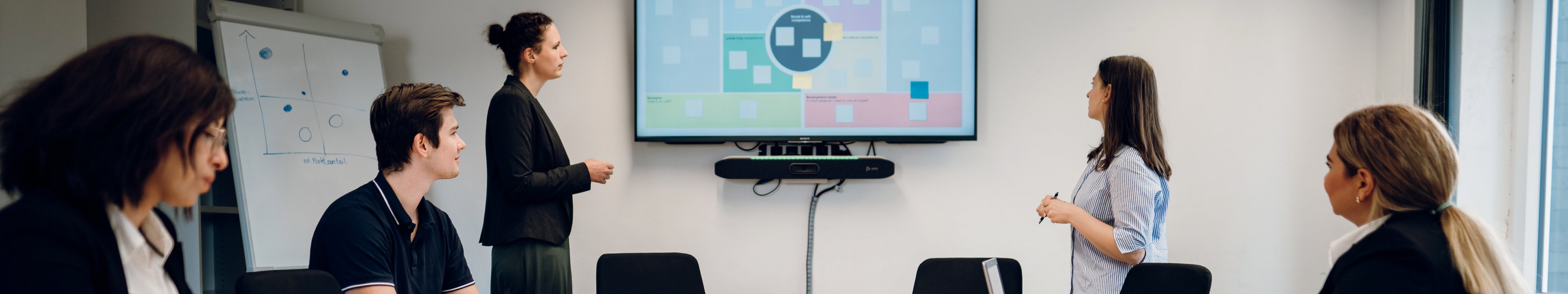 Studierende diskutieren in einem Seminarraum. Im Hintergrund ist eine Präsentation zu sehen. 