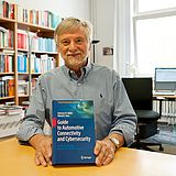 Person an einem Tisch hält ein Buch in der Hand