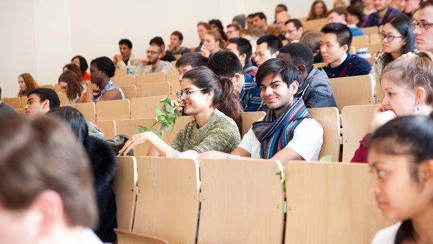 Studierende sitzen im Hörsaal, eine Person lächelt in die Kamera