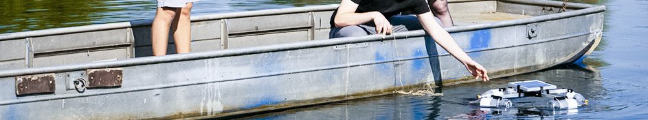 Drei Personen in einem Boot lassen ein Gerät ins Wasser
