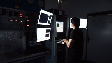 Eine Person arbeitet in einem dunklen Labor an einem Computer mit mehreren Bildschirmen