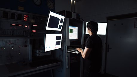 Eine Person arbeitet in einem dunklen Labor an einem Computer mit mehreren Bildschirmen