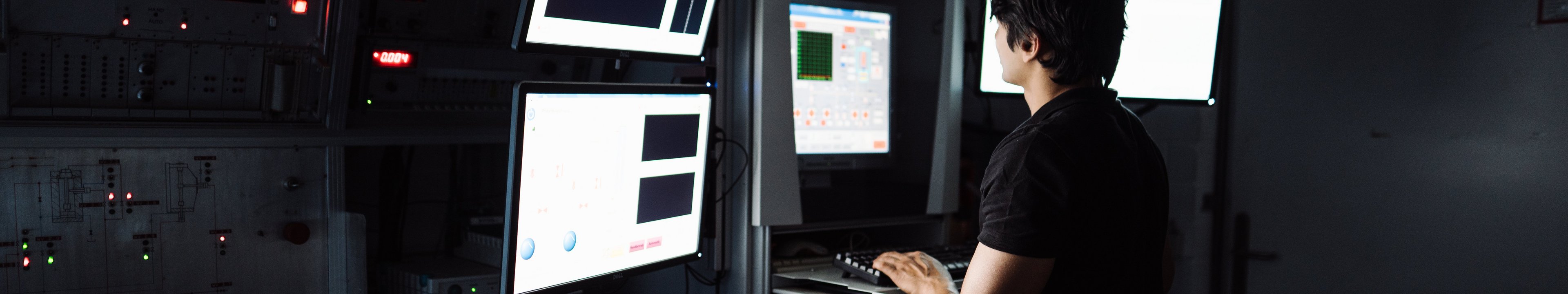 Eine Person arbeitet in einem dunklen Labor an einem Computer mit mehreren Bildschirmen