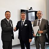 Menschen stehen nebeneinander in einem Raum vor einem Fernseher