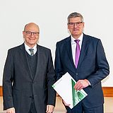 Person hält ein Dokument in der Hand und steht neben einer Person
