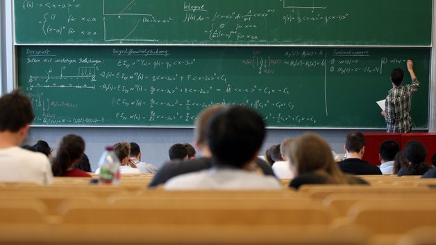 Dozent schreibt Formel an eine Tafel im Hörsaal