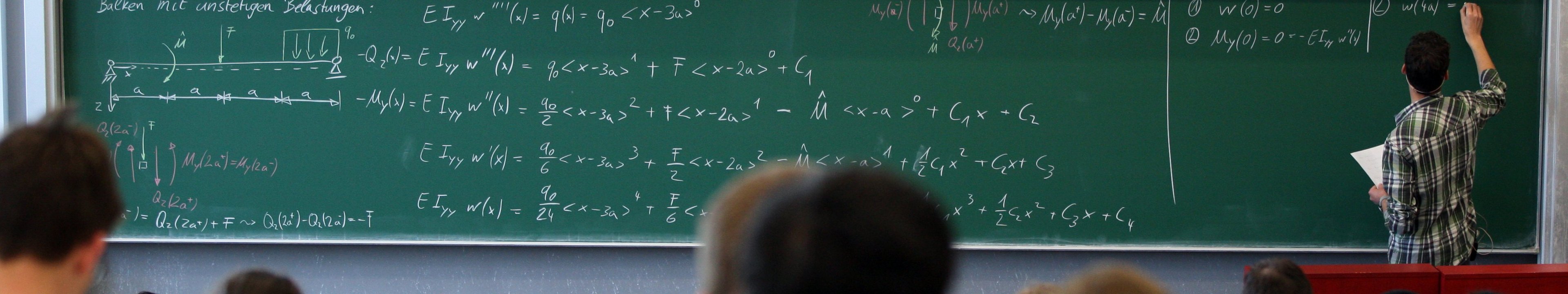 Dozent schreibt Formel an eine Tafel im Hörsaal