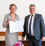 Person mit einer Urkunde steht neben einer Person