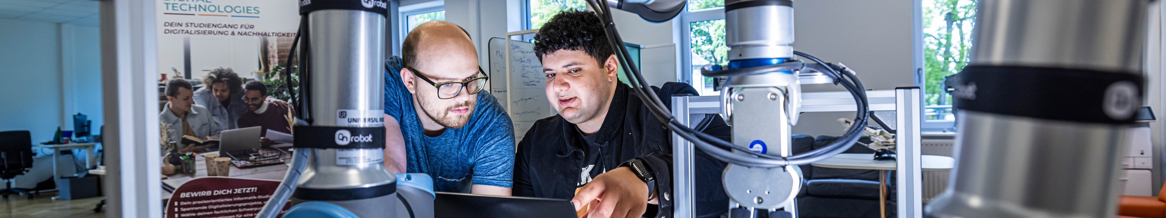 Studierende programmieren einen Roboterarm.