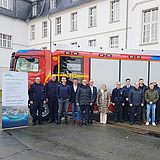 Menschen stehen in einer Reihe vor einem Feuerwehrauto.
