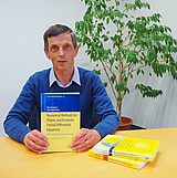 Eine Person an einem Tisch hält ein Buch in der Hand