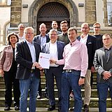 Zwei Personen halten ein Dokument und stehen neben anderen auf einer Treppe